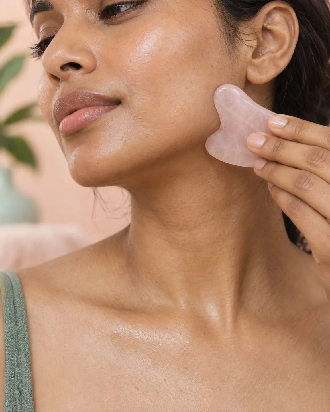 Hand gliding a rose quartz gua sha stone along the jawline toward the ear